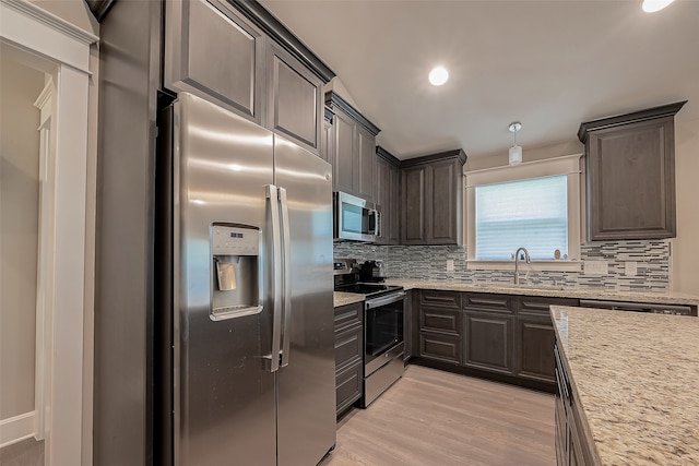 kitchen with stainless steel appliances, decorative backsplash, sink, light stone counters, and light hardwood / wood-style floors