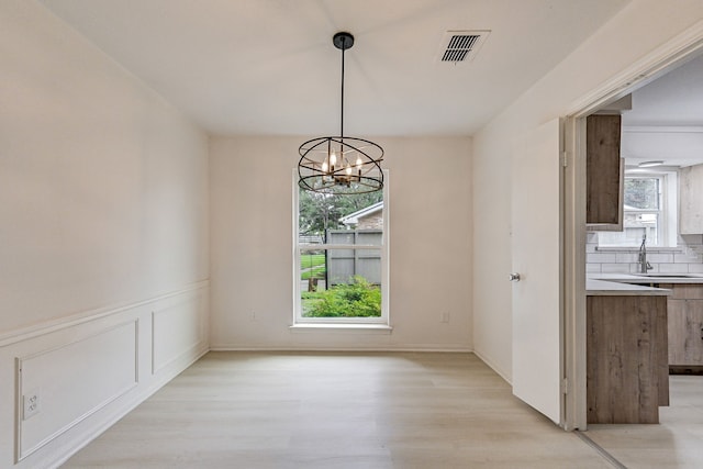 unfurnished dining area featuring light wood-type flooring, sink, and a notable chandelier