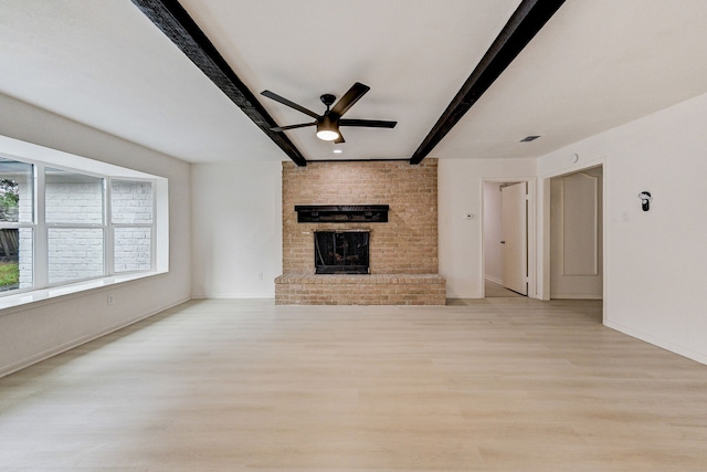 unfurnished living room featuring ceiling fan, beamed ceiling, a fireplace, and light hardwood / wood-style flooring