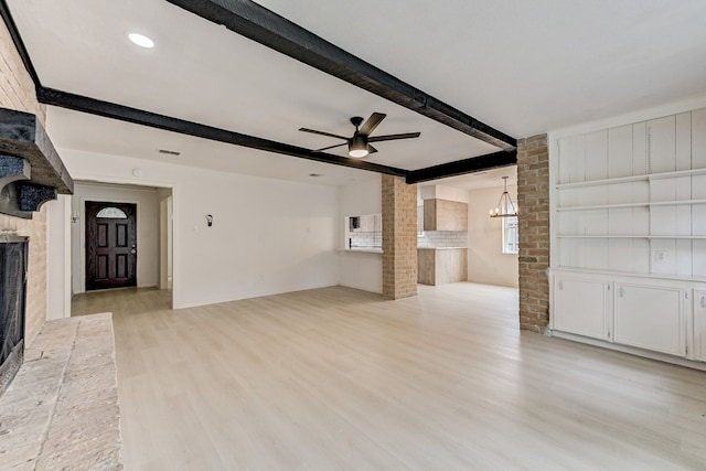 unfurnished living room with ceiling fan with notable chandelier, a brick fireplace, beamed ceiling, and light wood-type flooring