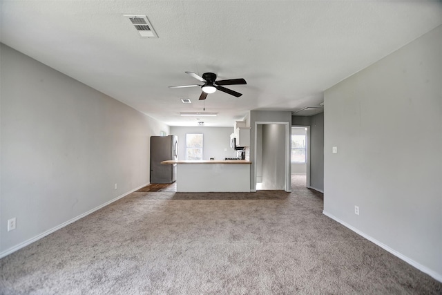 unfurnished living room with ceiling fan, carpet flooring, and a textured ceiling