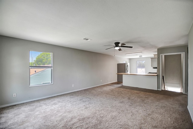 unfurnished living room with ceiling fan, a textured ceiling, a healthy amount of sunlight, and carpet