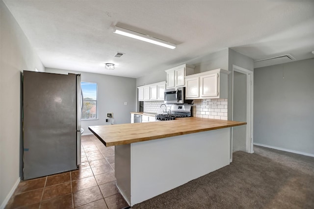 kitchen with appliances with stainless steel finishes, butcher block counters, white cabinetry, tasteful backsplash, and dark tile patterned flooring