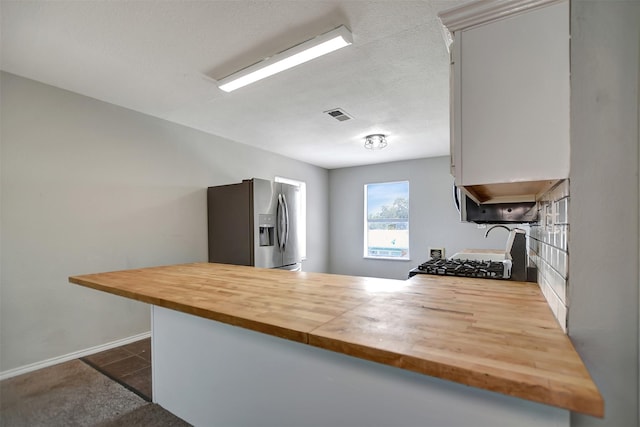 kitchen with stainless steel refrigerator with ice dispenser, stove, wood counters, and kitchen peninsula