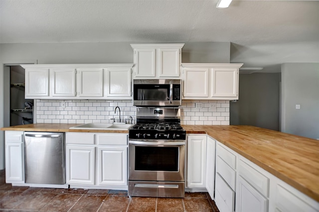 kitchen featuring sink, butcher block countertops, white cabinets, stainless steel appliances, and backsplash