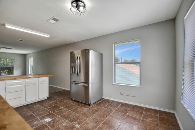 kitchen featuring butcher block countertops, plenty of natural light, white cabinets, and stainless steel refrigerator with ice dispenser