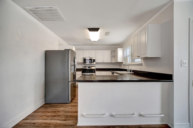 kitchen with sink, white cabinets, hardwood / wood-style flooring, kitchen peninsula, and stainless steel appliances