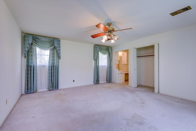 unfurnished bedroom featuring a closet, light colored carpet, ensuite bathroom, and ceiling fan