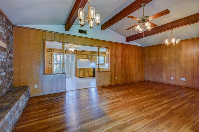 unfurnished living room featuring lofted ceiling with beams, wood walls, ceiling fan with notable chandelier, and light hardwood / wood-style flooring