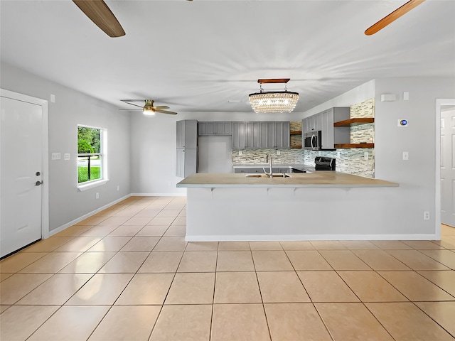 kitchen with gray cabinets, hanging light fixtures, ceiling fan with notable chandelier, decorative backsplash, and electric range oven