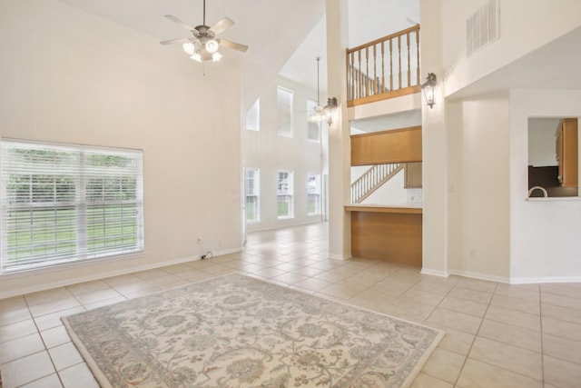 unfurnished living room with light tile patterned floors, a towering ceiling, and ceiling fan