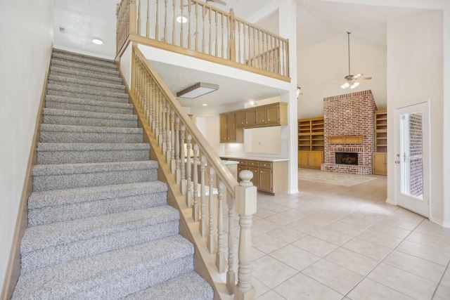 stairway with a fireplace, high vaulted ceiling, tile patterned flooring, ceiling fan, and built in shelves