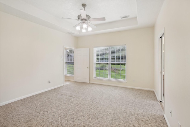 unfurnished room with ceiling fan, a raised ceiling, and light carpet