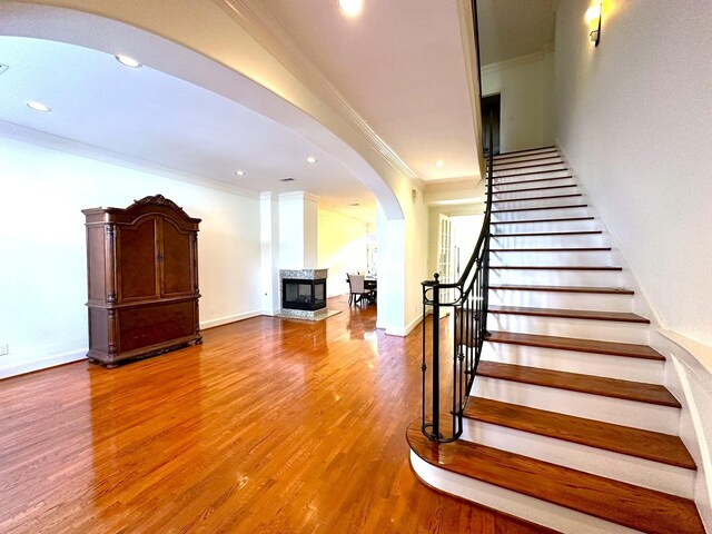 staircase featuring light wood-type flooring, a multi sided fireplace, and ornamental molding