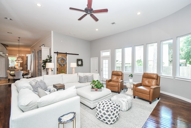 living room featuring a wealth of natural light, ceiling fan with notable chandelier, hardwood / wood-style flooring, and a barn door