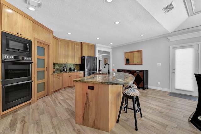 kitchen featuring sink, a kitchen breakfast bar, a kitchen island with sink, light hardwood / wood-style floors, and black appliances