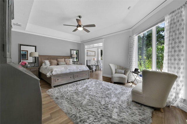 bedroom with hardwood / wood-style floors, ornamental molding, a raised ceiling, and ceiling fan