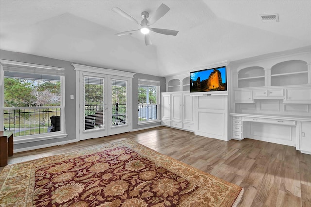 living room featuring built in shelves, vaulted ceiling, light hardwood / wood-style flooring, a textured ceiling, and ceiling fan