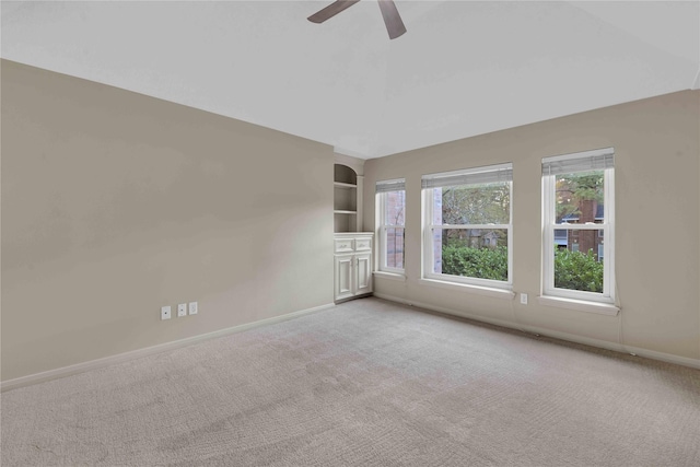 spare room with light carpet, ceiling fan, and built in shelves