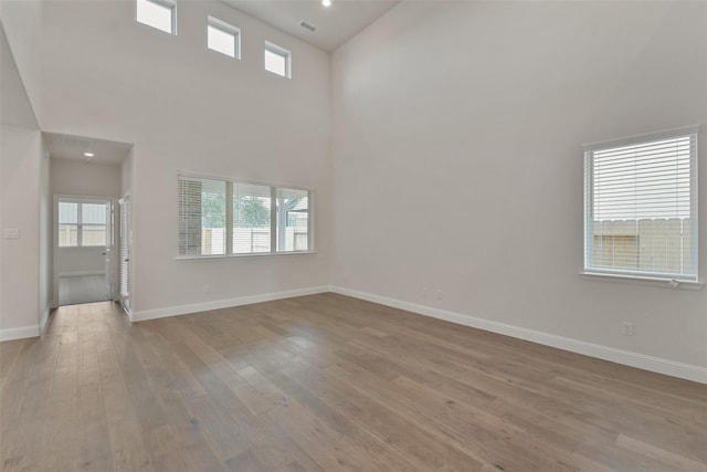 spare room with a healthy amount of sunlight, light hardwood / wood-style floors, and a towering ceiling