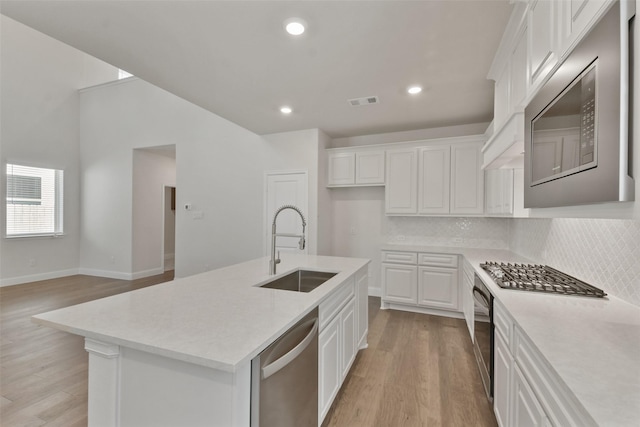 kitchen with an island with sink, sink, white cabinets, stainless steel appliances, and light hardwood / wood-style flooring