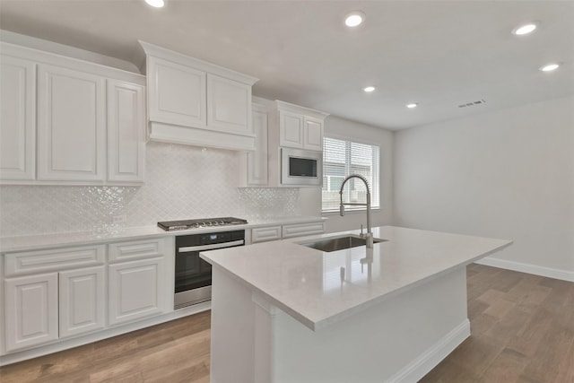 kitchen with stainless steel appliances, sink, a center island with sink, and white cabinets