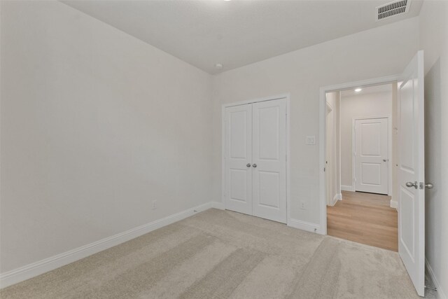 unfurnished bedroom with light colored carpet and a closet