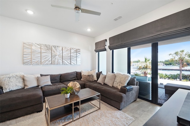 living room with a water view, light wood-type flooring, and ceiling fan