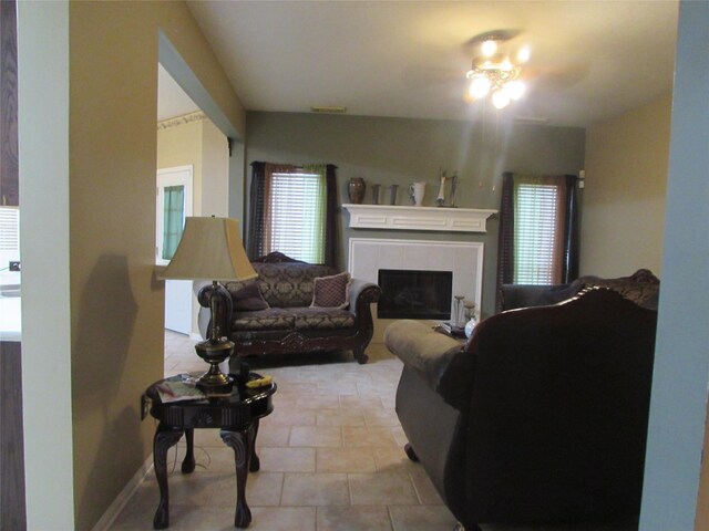 tiled living room with a tile fireplace and ceiling fan