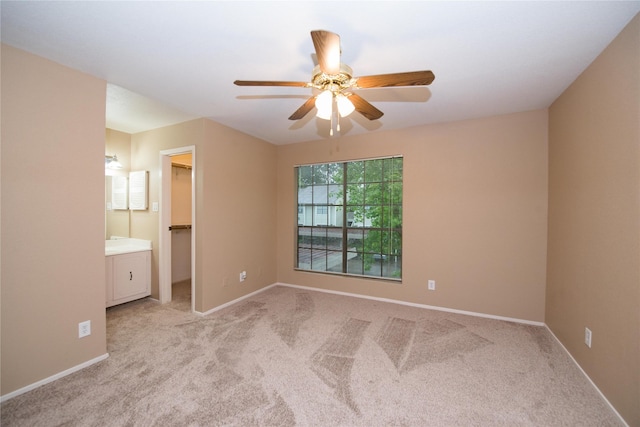 unfurnished bedroom featuring a walk in closet, light colored carpet, ceiling fan, and ensuite bathroom