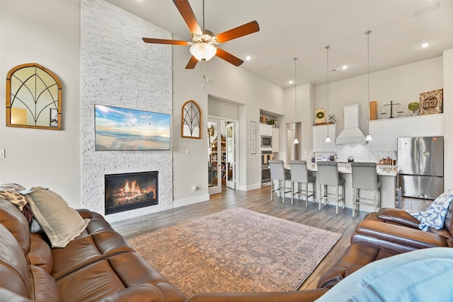 living room featuring a stone fireplace, a towering ceiling, dark hardwood / wood-style flooring, and ceiling fan