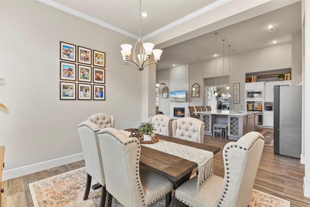 dining room featuring an inviting chandelier, sink, light wood-type flooring, a large fireplace, and ornamental molding