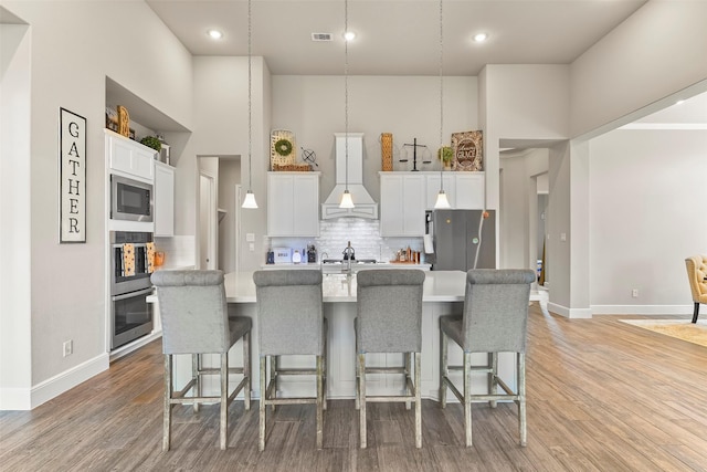 kitchen with white cabinetry, custom range hood, stainless steel appliances, light hardwood / wood-style floors, and decorative backsplash