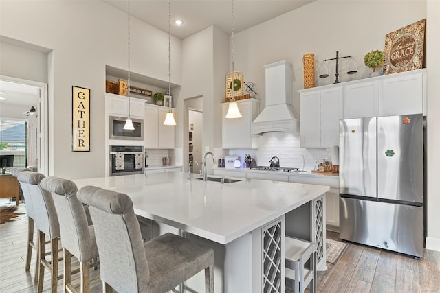 kitchen with decorative backsplash, appliances with stainless steel finishes, custom exhaust hood, and an island with sink