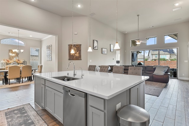 kitchen with stainless steel dishwasher, ceiling fan with notable chandelier, sink, light hardwood / wood-style floors, and a kitchen island with sink