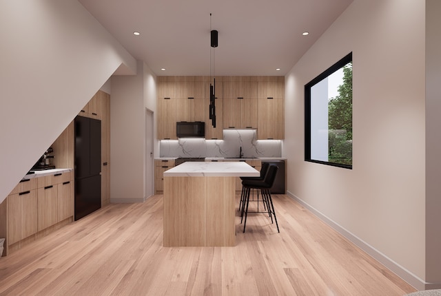 kitchen with light wood-type flooring, a breakfast bar, black appliances, decorative light fixtures, and a center island