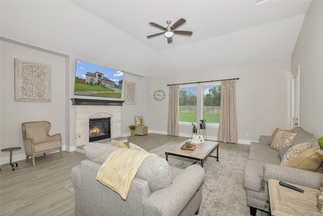 living room with a stone fireplace, light wood-type flooring, and ceiling fan