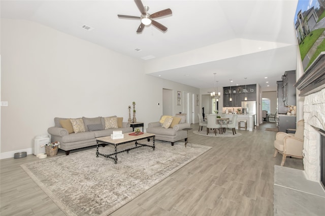 living room featuring a fireplace, ceiling fan with notable chandelier, light hardwood / wood-style flooring, and vaulted ceiling