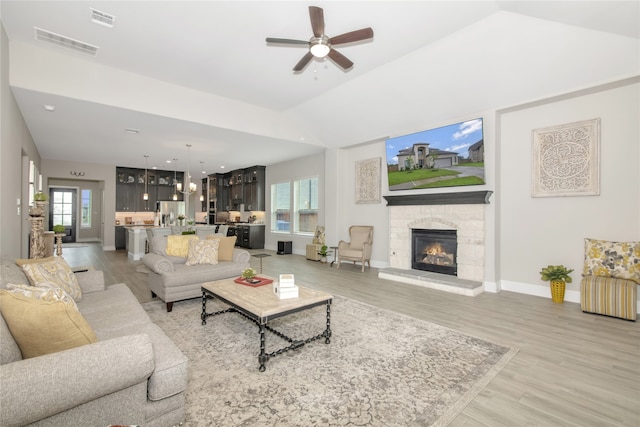 living room with light hardwood / wood-style floors, a wealth of natural light, a stone fireplace, and ceiling fan