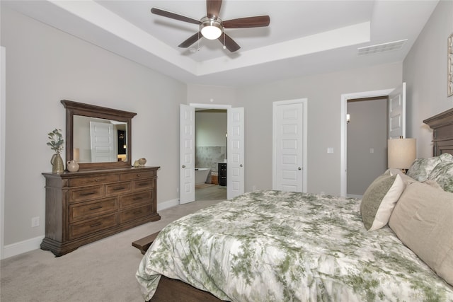 carpeted bedroom with ceiling fan, ensuite bath, and a tray ceiling