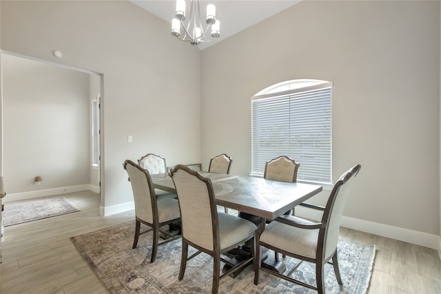 dining area with light hardwood / wood-style flooring, an inviting chandelier, and high vaulted ceiling