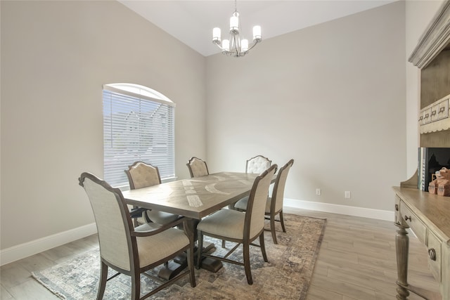 dining area with light hardwood / wood-style floors, an inviting chandelier, and high vaulted ceiling