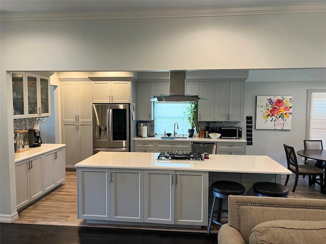 kitchen featuring light wood-type flooring, stainless steel appliances, sink, island exhaust hood, and gray cabinetry