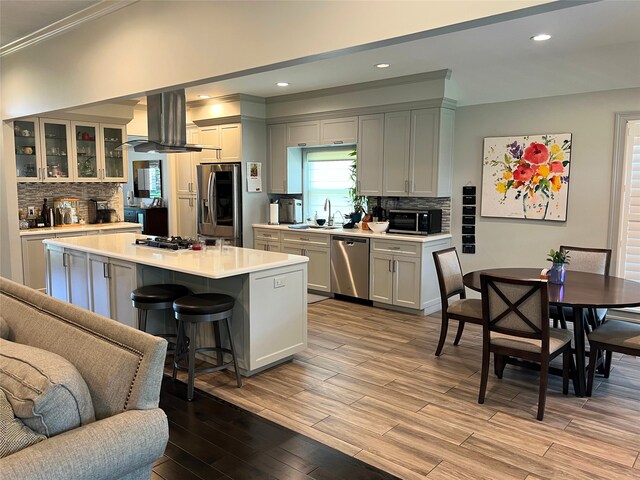 kitchen with light hardwood / wood-style floors, crown molding, island range hood, stainless steel appliances, and a center island