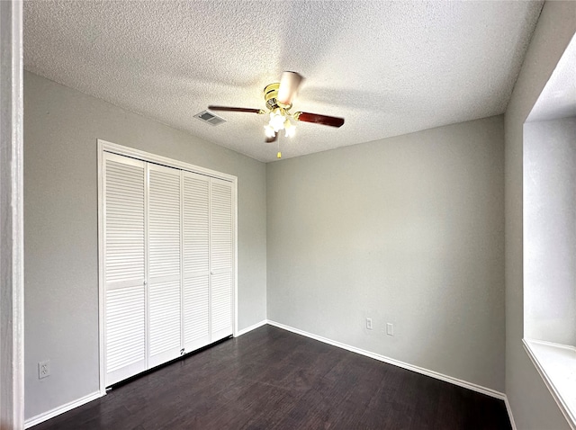 unfurnished bedroom with a textured ceiling, ceiling fan, dark wood-type flooring, and a closet