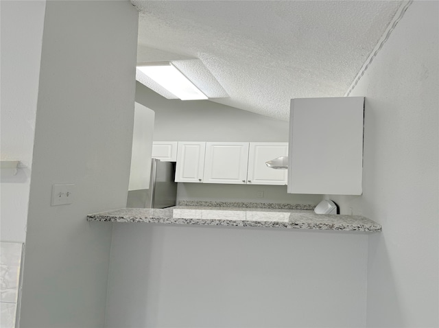 kitchen featuring light stone counters, white cabinets, ventilation hood, stainless steel refrigerator, and vaulted ceiling