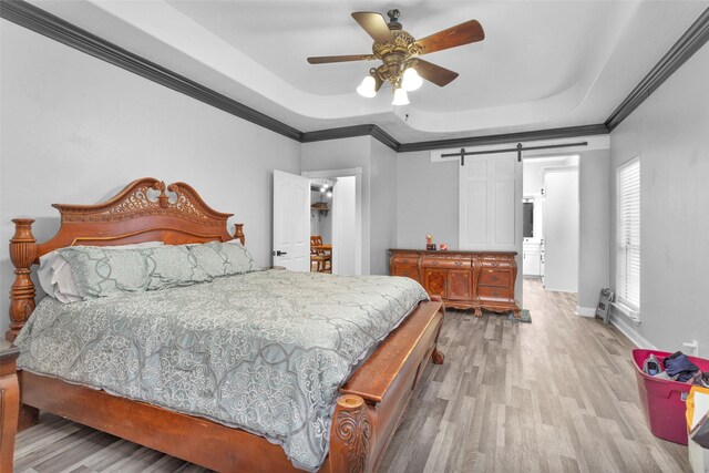 bedroom featuring wood-type flooring, a raised ceiling, a barn door, and ceiling fan