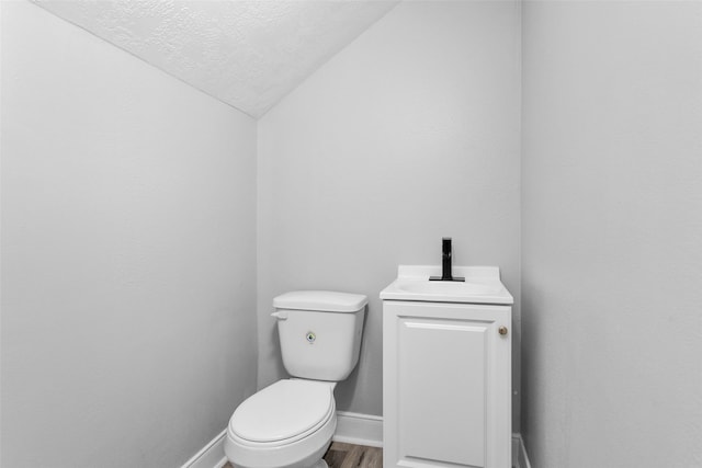 bathroom with a textured ceiling, lofted ceiling, toilet, vanity, and hardwood / wood-style flooring