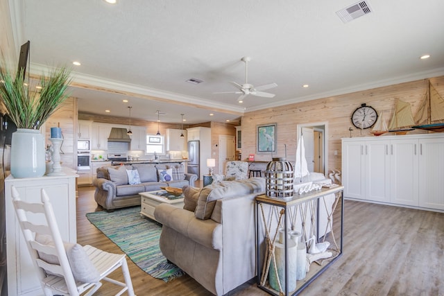 living room with ceiling fan, crown molding, light hardwood / wood-style flooring, and wood walls