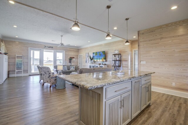 kitchen with light stone countertops, a center island, hanging light fixtures, ceiling fan, and dark wood-type flooring